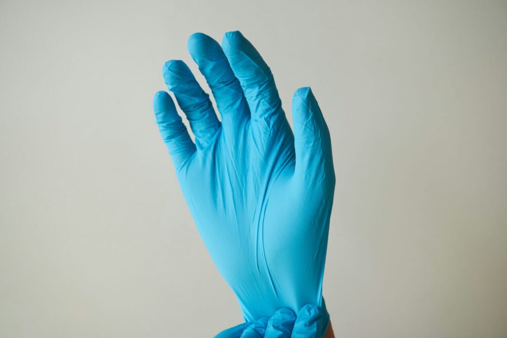 person pulling on a surgical/cleaning glove with a neutral background